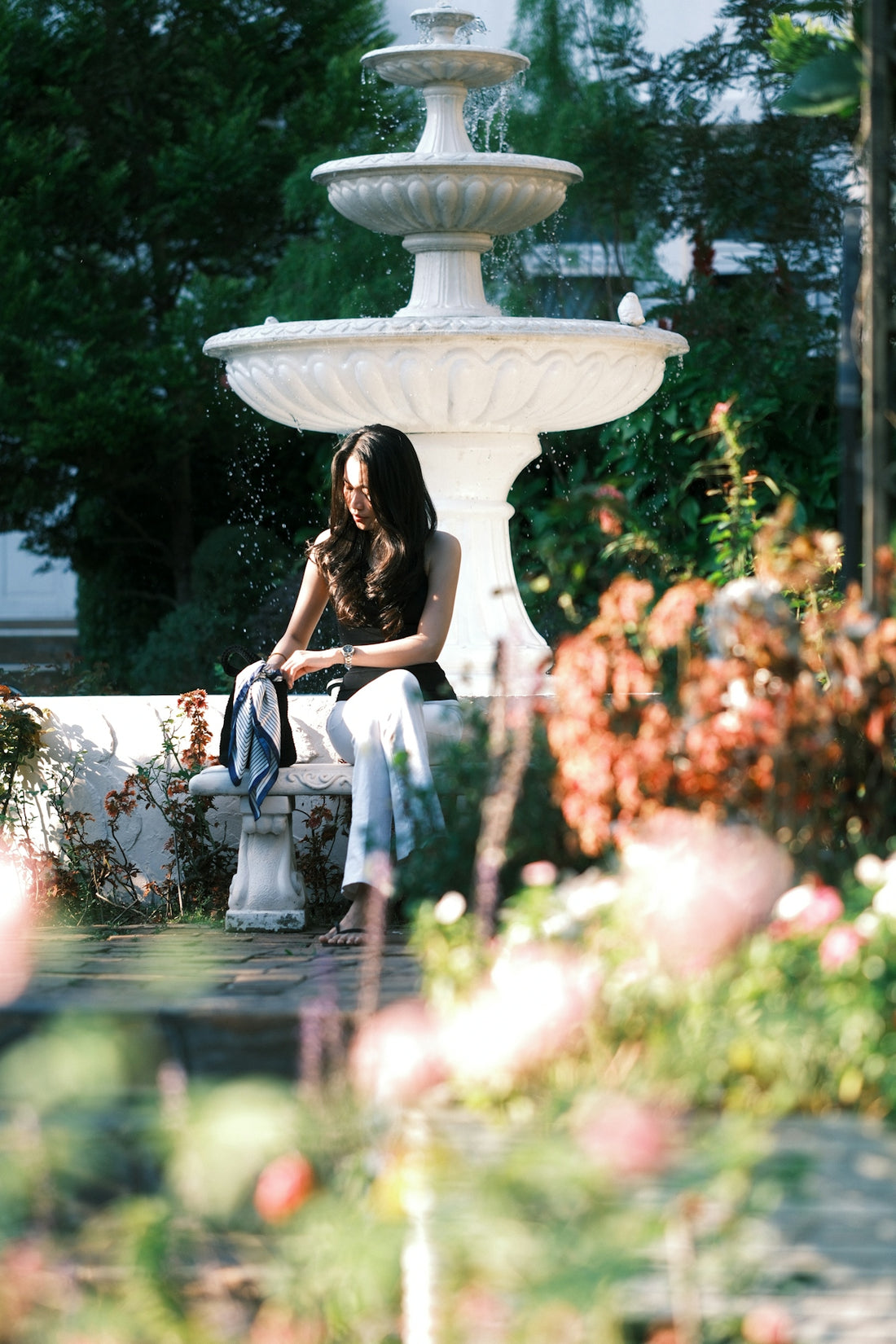 A woman sits on a bench near a fountain.