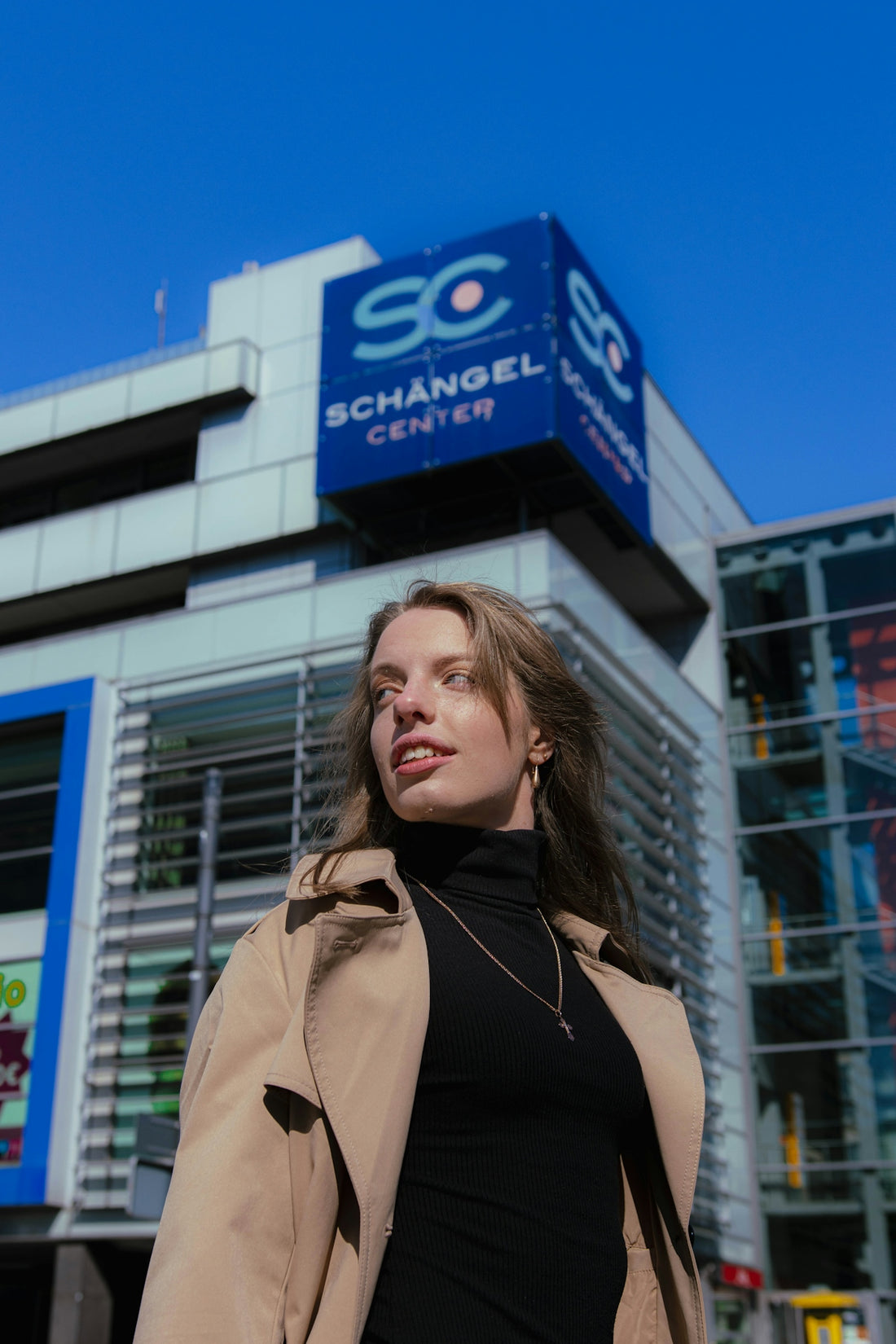 Young woman in trench coat in front of building
