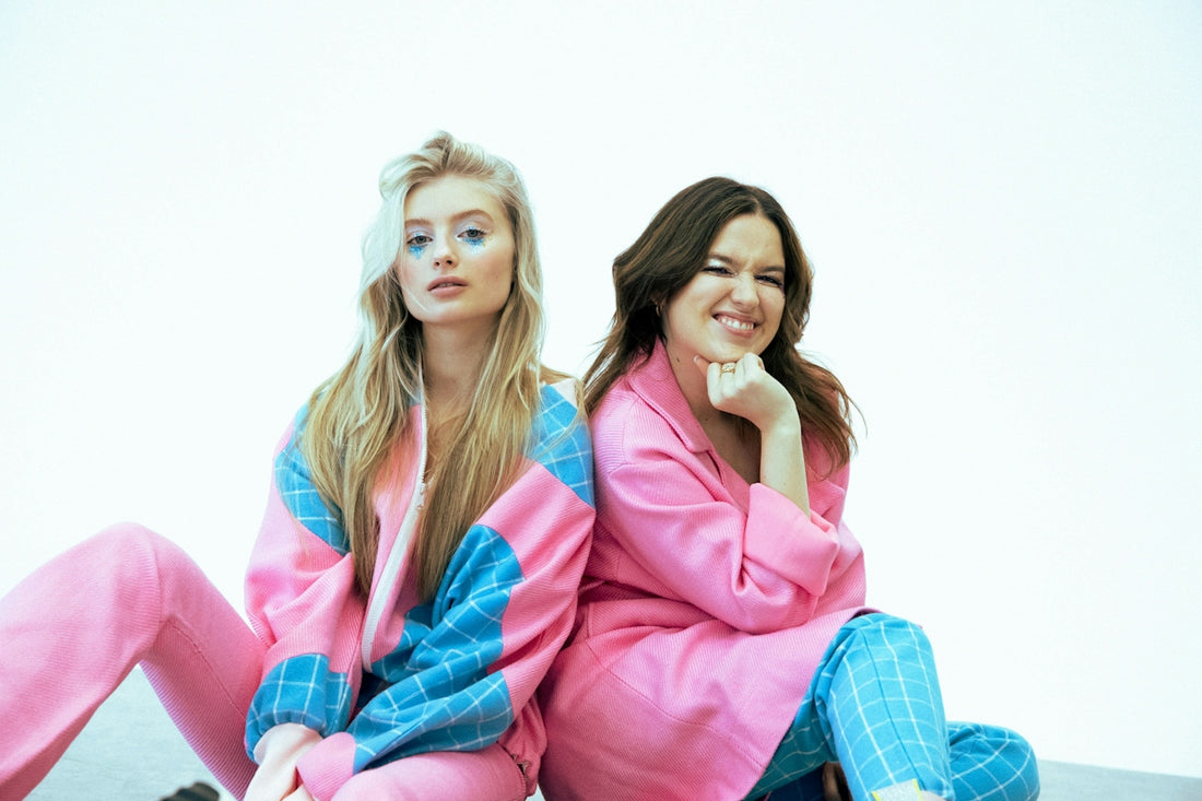 Two women in pink and blue outfits back-to-back.