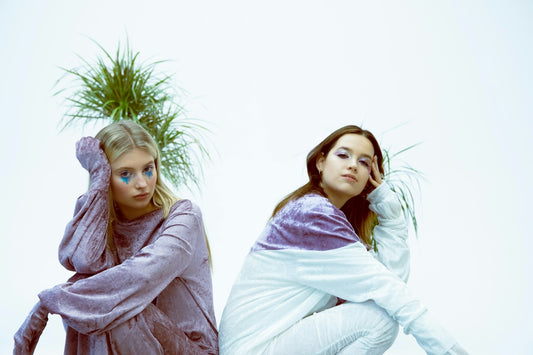 Two young women sitting with green foliage on white