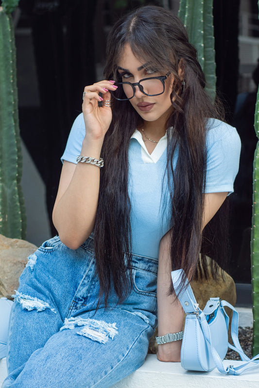 Young woman in blue outfit holding glasses near cacti